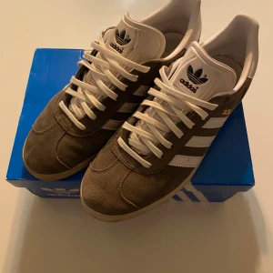 Adidas Gazelle grå/vit - Adidas gazelle, strl 43, bra skick men smutsiga kan rengöra vid efterfråga, bara att höra av sig vid frågor och funderingar. Box ingår ej