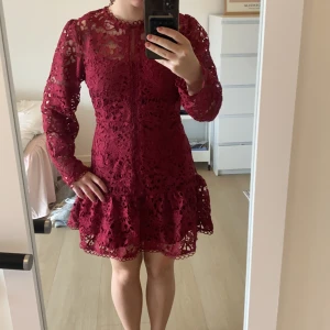 Vinröd spetsklänning med volang - Säljer en vinröd kortklänning med långärmade ärmar och vacker spetsdetalj. Klänningen har rund hals, figurnära passform och en volang nedtill. Dragkedja i ryggen för enkel påklädning. Perfekt höst/jul klänning. Bara använd en gång(julafton)