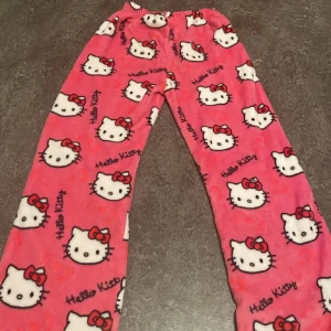 Hello Kitty rosa mjukisbyxor - Supergulliga rosa mjukisbyxor med Hello Kitty-motiv över hela byxorna. Byxorna har resår i midjan och är gjorda i ett mjukt och mysigt fleecematerial. Perfekta för chill dagar hemma eller sleepovers med kompisarna.