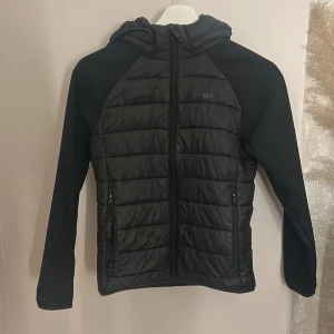 Svart pufferjacka från Everest - Svart pufferjacka från Everest med huva och hel dragkedja. Jackan har quiltad framsida och rygg, släta ärmar och två fickor med dragkedja✨(ops.. dragkedjan på höger sida är trasig och går därmed inte att stänga) pris kan diskuteras!