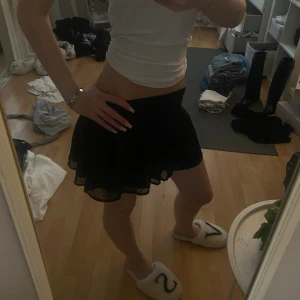 Svart prickig volangkjol Gina Tricot - Säljer en svart kortkjol från Gina Tricot med volangkant och transparent lager med små prickar. Kjolen har en flowy passform och resår i midjan, perfekt för dig som gillar en söt och trendig stil.