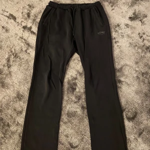 Svarta mjukisbyxor från BOSS - Svarta mjukisbyxor från BOSS med dragsko i midjan och två sidofickor. Byxorna har en stilren logga på vänster sida och är tillverkade i ett mjukt material som känns skönt mot huden. Perfekta för en chill look och enkel att matcha med hoodies eller t-shirts.