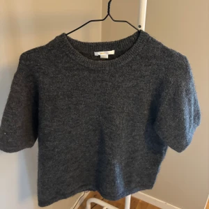 Mörkgrå stickad tröja Gina Tricot - Mysig mörkgrå stickad tröja från Gina Tricot med korta ärmar och rund halsringning. Perfekt för lager-på-lager och passar till både jeans och kjol. Enkel och stilren design som funkar året runt.