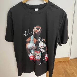 Svart t-shirt med boxartryck, M - Svart t-shirt i 100% polyester med stort tryck av en boxare med bälten och röda handskar på framsidan. Rund hals och korta ärmar. Snygg och sportig vibe, perfekt för dig som gillar boxning eller coola motiv.