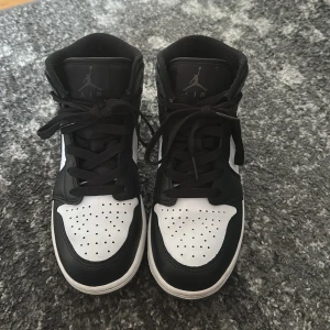 Nike Air Jordan 1 svart/vit sneakers - Säljer ett par Nike Air Jordan 1 sneakers i svart, vitt och mörkgrått skinn. Klassisk high-top modell med svart swoosh, perforerad tå och snörning. Ikonisk Jordan-logga på sidan och tungspets. Perfekta för dig som gillar streetstyle och vill sticka ut. Använda ett par gånger men är i jätte bra skick. Kommer tyvärr inte med själva boxen eftersom jag råkade slänga den då jag inte trodde skorna skulle säljas.