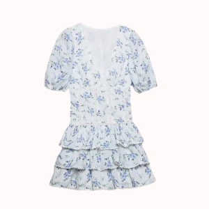 Blommig kortklänning med volanger - Supersöt kortklänning med ljusblå och lila blommor på vit botten. Klänningen har puffiga korta ärmar, v-ringad hals och flera lager volanger i kjolen. Spetsdetaljer längs sömmarna ger extra romantisk vibe. Perfekt för sommarens alla tillfällen! Säljer då den var för liten och aldrig använd.