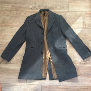 Grå kavaj från Morris Stockholm - Säljer en stilren grå kavaj från Morris Stockholm med klassisk passform. Kavajen har tre knappar framtill, två fickor med lock och en bröstficka. Fodret är lyxigt guldigt och materialet känns mjukt och gediget, troligen ullblandning. Perfekt för dig som vill ha en tidlös look.