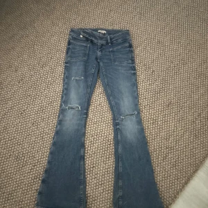 Blå bootcut jeans med slitningar - Snygga blå jeans med bootcut-modell och slitna detaljer vid knäna. Jeansen har klassiska fickor fram och bak samt en lätt tvättad look. Perfekta för dig som gillar en retrostil med lite edge.