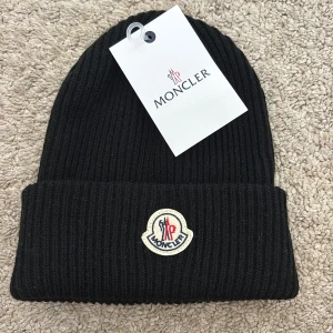 Mössa - Svart ribbstickad mössa med klassisk uppvikt kant och broderad logotyp framtill. Tillverkad i mjukt material som håller dig varm och ger en clean look. Perfekt accessoar för kyliga dagar och snygg till streetwear.