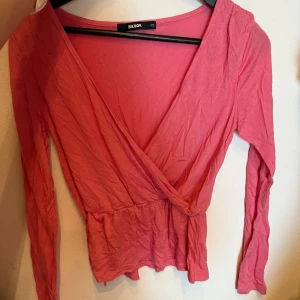 Rosa omlottopp från Bik Bok - Säljer en söt rosa omlottopp från Bik Bok i storlek XS. Toppen har lång ärm, v-ringning och ett peplumliknande fall vid midjan. Perfekt för dig som gillar en feminin och trendig stil. Materialet är mjukt och skönt bomull.