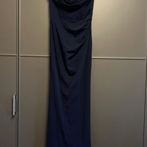 Marinblå långklänning med drapering - Säljer en elegant marinblå långklänning med snygg drapering framtill. Klänningen har en enkel och stilren design, perfekt för dig som gillar klassiska plagg. Modellen är axelbandslös och har en smickrande passform.