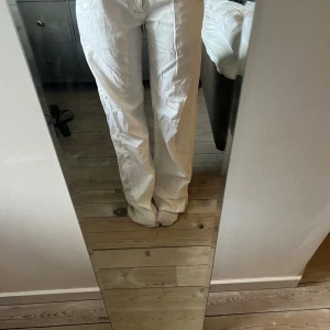 Vita raka byxor från Koola Anna - Vita byxor från Koola Anna med raka ben och normal passform. Snygga detaljer med rosa broderad logga baktill och rosa sömmar. Byxorna har dragkedja och dubbla knappar framtill samt klassiska bakfickor. Perfekta för en fräsch och clean look. De är långa på mig som är 170 cm lång och är lite slitna nere vid fötterna. Kan skicka bild om man vill.