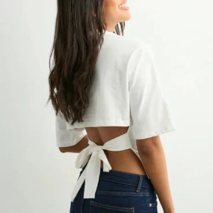 Vit topp från Nelly  - Säljer en vit  topp med korta ärmar och öppen rygg som knyts med en bred rosett baktill. Toppen har en stilren och modern look, perfekt för dig som gillar att sticka ut med detaljer. Materialet känns mjukt och lätt mot huden.