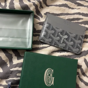 Grå plånbok med mönster  - Snygg grå plånbok med klassiskt mönster i vitt och grått. Plånboken har flera fack för kort och är tillverkad i skinn med en stilren design. Perfekt för dig som vill ha något exklusivt och trendigt i fickan.