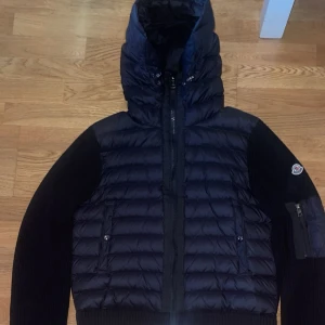 Svart Moncler pufferjacka med huva - Säljer en svart pufferjacka från Moncler i storlek S/M. Jackan har stickade ärmar, quiltad kropp och stor huva. Dragkedja framtill och fickor med knappstängning. Moncler-logga på ärmen och ribbad nederkant. Perfekt för dig som gillar exklusiva märken och snygg design. Priset kan diskuteras 