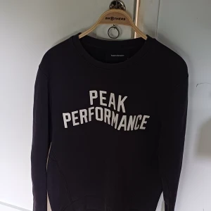 Svart Peak Performance sweatshirt M - Svart sweatshirt från Peak Performance i storlek M med vit logotyptext på bröstet. Tröjan har rund hals, långa ärmar och är tillverkad i mjuk bomullsmix. Perfekt för chill dagar eller när du vill ha en clean och sportig look.