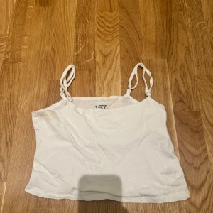 Vit croppad linnetopp från Lager 157 - Säljer en enkel och fräsch vit croppad linnetopp från Lager 157. Toppen har smala axelband som är justerbara, avslappnad passform. Tillverkad i mjuk bomull med lite stretch för extra komfort. Perfekt till sommaren och lätt att matcha med allt.