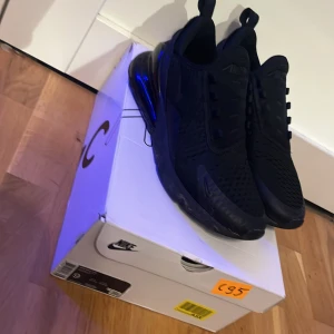 Nike Air Max 270 helsvarta sneakers - Nike Air Max 270 sneakers i helsvart med stor synlig Air-enhet i hälen. Ovandel i mesh och syntet för bra andningsförmåga och komfort. Snygg, sportig look med rund tå och platt sula. Perfekta för dig som gillar stilrena och moderna sneakers.