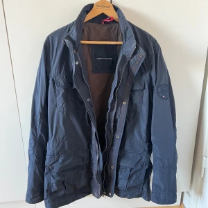 Mörkblå vår/höstjacka Tommy Hilfiger M - Mörkblå vår/höstjacka från Tommy Hilfiger i storlek M. Jackan har dubbel dragkedja, tryckknappar framtill och hög krage. 