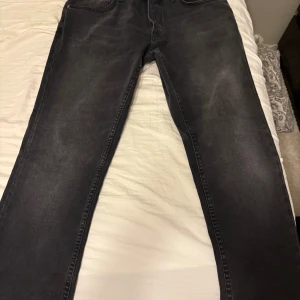 Svarta jeans från Nudie Jeans Co, 34/34 - Snygga svarta jeans från Nudie Jeans Co i storlek 34/34. Jeansen har klassisk femficksdesign, svarta sömmar och en något tvättad look. Helt nya typ använda max 2 gånger, Perfekt passform med raka ben och diskret logga på bakfickan. Tillverkade i mjukt och slitstarkt bomullstyg.