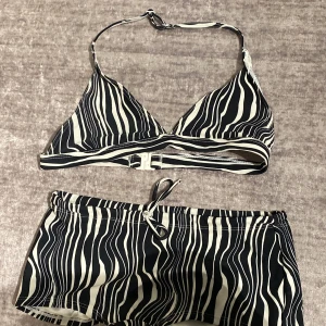 Zebramönstrad bikini med shorts - Snygg bikini med zebramönster i svart och vitt. Överdelen har trekantskupor med knyt i nacken och spänne i ryggen. Underdelen är ett par shorts med snörning framtill. Perfekt för strandhäng eller poolparty!