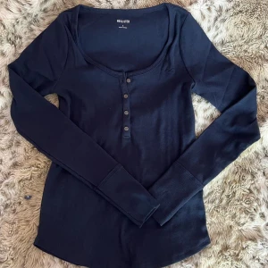 SÖKER Mörkblå långärmad topp Hollister - SÖKER I S ELLER XS - Mörkblå långärmad topp från Hollister med rundad urringning och knappdetaljer framtill. Tillverkad i mjuk bomull med ribbad struktur. Perfekt för lager-på-lager och enkel att styla till jeans eller kjol.