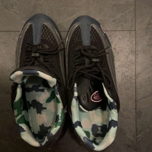 Nike Air Max sneakers med camo-detaljer - Unika Nike Air Max sneakers i svart och mörkblått med coola camo-mönstrade innersulor i grönt, blått och vitt. Skorna har rosa detaljer och synlig Air Max-dämpning i sulan. Ovandelen är i mesh och syntet med snörning för perfekt passform.