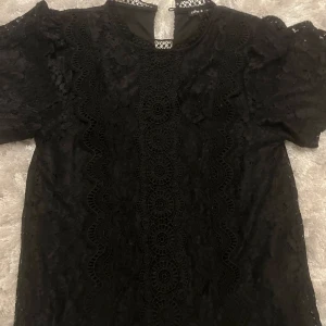 Svart spetsblus från Cable & Gauge - Supersnygg svart blus från Cable & Gauge med vackra spetsdetaljer och broderade mönster Perfekt för dig som gillar en elegant och trendig look.