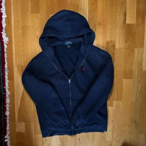 Polo Ralph Lauren zip hoodie   - Hej! Säljer nu mörkblå zip hoodie från Polo Ralph Lauren med dragkedja och huva. Tröjan har det klassiska röda Polo-logot på bröstet och är tillverkad i mjuk bomull. Den kom aldrig till använd pågrund av fel storlek så den är i topp skick: 10/10 Storlek: S Nypris: 1200. Skriv vid frågor eller funderinger.