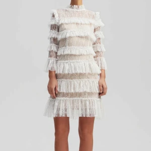 Vit spetsklänning med volanger by Malene Birger  - Supersnygg kort klänning i vit spets med transparenta partier och flera lager volanger. Klänningen har lång ärm, hög hals och ett romantiskt mönster i spetsen. Materialet är lätt och ger en lyxig känsla, perfekt för dig som vill sticka ut med en unik look.