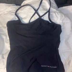 top - Snygg svart linnetopp från Tommy Hilfiger med tunna axelband som korsas i ryggen. Toppen har en liten logotyp nertill och meshdetaljer vid axlarna. Perfekt för en sportig och stilren look.