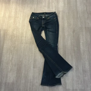 True Religion bootcut jeans blå - Snygga blå jeans från True Religion med bootcut passform och klassiska kontrastsömmar. Bakfickorna har lock och silverfärgade knappar med märkets logga. Jeansen har låg midja och är tillverkade i slitstarkt denimtyg. Lite slitna längst ner på byxorna men inget man tänker på när man har på sig dem. Skriv om ni vill ha bild på hur dem sitter på eller andra frågor 💞 