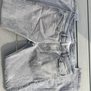 Grå Diesel jeans - Säljer ett par gråa Diesel Thavar XP jeans med slim passform. Jeansen har klassisk femficksdesign, snygga slitningar och diskret tvättad look. Perfekta för dig som gillar en smal siluett och vill ha ett par stilrena jeans med edge.