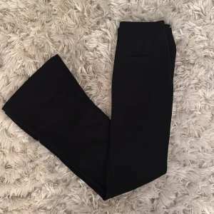 Svarta bootcut kostymbyxor SHEIN S - Svarta kostymbyxor från SHEIN i storlek Tall S. Byxorna har bootcut-ben, hög midja och två dekorativa fickor fram. Snygg och stilren modell i ett mjukt, slätt material som ger en dressad look.