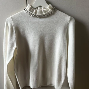 Vit stickad tröja med pärlor Reserved - Supersöt vit stickad tröja från Reserved med långa ärmar och ribbad hög krage dekorerad med stora glittrande pärlor. Perfekt för dig som vill ha något extra till vintern eller julen. Snygg och stilren modell som lyfter hela outfiten.