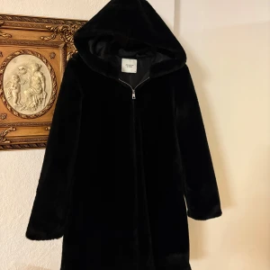 Svart pälsjacka med huva  - Mysig svart pälsjacka från Jacqueline de Yong i storlek M. Jackan har en stor huva, dragkedja framtill och är helsvart med mjuk pälsimitation. Perfekt för kalla dagar när du vill vara både varm och snygg. Perfekt nu för vintern, stilig och håller dig varm, mysig päls. Använd 1 gång. 