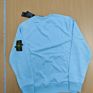Ljusblå Stone Island sweatshirt M - Helt oanvand sprillans ny Snygg ljusblå sweatshirt från Stone Island i bomull. Klassisk rund hals, ribbade muddar och ikonisk logga på vänster ärm. Perfekt för dig som vill ha en stilren och trendig tröja med streetkänsla.❄️