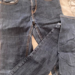 Blå jeans från Denim by Lindex - Säljer ett par klassiska blå jeans från Denim by Lindex. Jeansen har raka ben, fem fickor och kontrastsömmar i orange. Tillverkade i mjukt denimtyg som sitter skönt hela dagen. Perfekta för dig som gillar en tidlös look.
