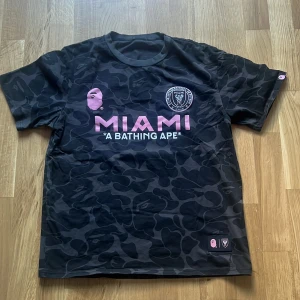 Inter Miami x BAPE camo fotbollströja - Snygg svart camo fotbollströja från Inter Miami och BAPE med rosa tryck, klubbmärke på bröstet och stor BAPE 93 på ryggen och den är använd endast en gång!