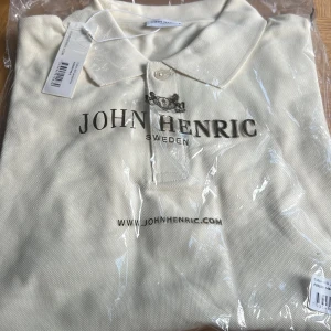 Vit pikétröja från John Henric - Helt ny fräsch vit pikétröja från John Henric Tröjan är gjord i mjuk bomull som känns skön mot huden. Perfekt för dig som gillar stilrena och enkla plagg med snygg passform. Nypris 600kr