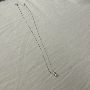 Silverhalsband med glittrande sten - Ett stilrent halsband i silverfärg med en tunn kedja och ett runt, glittrande hänge som fångar ljuset snyggt. Perfekt för dig som gillar minimalistiska smycken med en touch av elegans. Passar till alla tillfällen och är lätt att matcha med andra accessoarer.