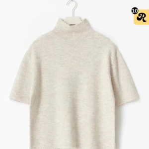 Beige stickad polotröja med kort ärm - Supersnygg beige stickad polotröja med korta ärmar och hög krage. Tröjan har en avslappnad passform och ribbade detaljer vid hals, ärmslut och nederkant. Perfekt att styla med kjol eller jeans för en clean look. Aldrig använd och med prislappen kvar. Även helt slutsåld i den storleken.