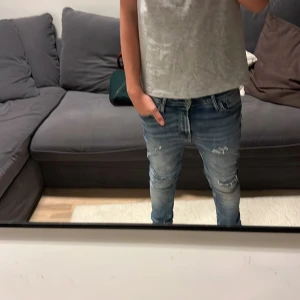 Blå slim fit jeans från Jack & Jones - Säljer ett par blå slim fit jeans från Jack & Jones med slitningar och snygga detaljer på knäna. Jeansen har klassisk femficksdesign, låg midja och är tillverkade i stretchig bomull för en bekväm passform. Perfekta för dig som gillar en modern och tight stil. Modellen på bild är 172. 