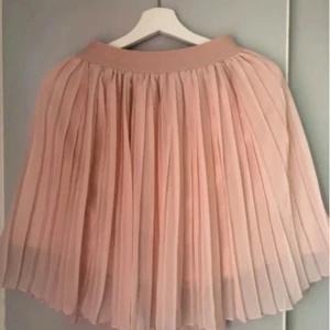 Plisserad ljusrosa kortkjol - Säljer en superfin plisserad kjol i ljusrosa med bred linning. Kjolen är kort och har ett flowigt, luftigt tyg som ger snygg volym. Perfekt för dig som gillar romantisk och feminin stil. Materialet känns lätt och skönt mot huden.