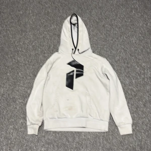 Vit hoodie från Peak Performance S - Vit hoodie från Peak Performance med svart logga framtill. Klassisk känguruficka, snörning i huvan och ribbade muddar. Finns en liten svart fläck på framsidan Ni står för frakt!