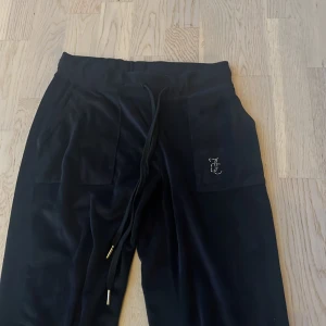 Svarta Juicy Couture mjukisbyxor - Svarta mjukisbyxor från Juicy Couture i mjuk velour med snörning i midjan och stora fickor fram. På ena fickan finns ett glittrigt JC-logotyp i strass och på baksidan står det 'Juicy' i stora bokstäver💓Bara använda få gånger därför är de i bra skick. Orginalpris 1500kr💓storlek S.