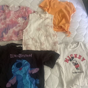 Fem trendiga toppar med tryck och färg - Säljer fem snygga toppar: en rosa-lila tie dye crop top med Dua Lipa-tryck, en ribbad ärmlös topp i ljusrosa tie dye, en orange kortärmad topp med knyt i sidan, en svart Lilo & Stitch t-shirt och en vit ribbad topp med Mickey Mouse-tryck. 75 för alla!💗