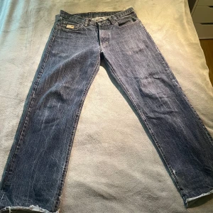 Vintage bape jeans - Vintage bape jeans i blå denim med coolt tryck av figur och stjärna på bakfickorna. Klassisk rak passform och normal midja. Jeansen har slitna benslut för en avslappnad vibe och är tillverkade i robust bomullsjeans.