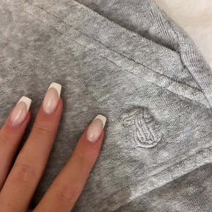 Grå mjukisbyxor från Juicy Couture - Grå mjukisbyxor från Juicy Couture med broderad logga på benet, stora fickor framtill och snörning i midjan. Byxorna har silverfärgade detaljer på fickorna och en skön loose passform. Perfekta för chill dagar eller när du vill vara extra comfy.