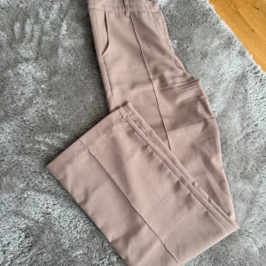 Beiga kostymbyxor med pressveck - Snygga beiga kostymbyxor med raka ben och pressveck framtill. Byxorna har fickor i sidorna och hällor för bälte. Materialet är mjukt och har en lätt stretch.